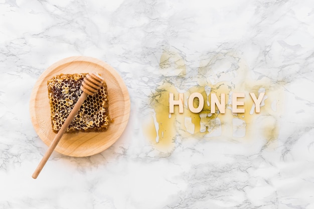 Honey text with honeycomb and dipper on wooden plate over the white marble backdrop