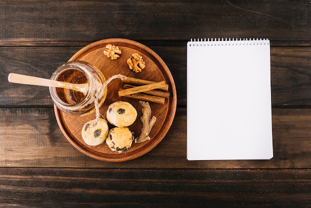 Honey; walnut; spices and cup cakes near spiral notepad on wooden surface