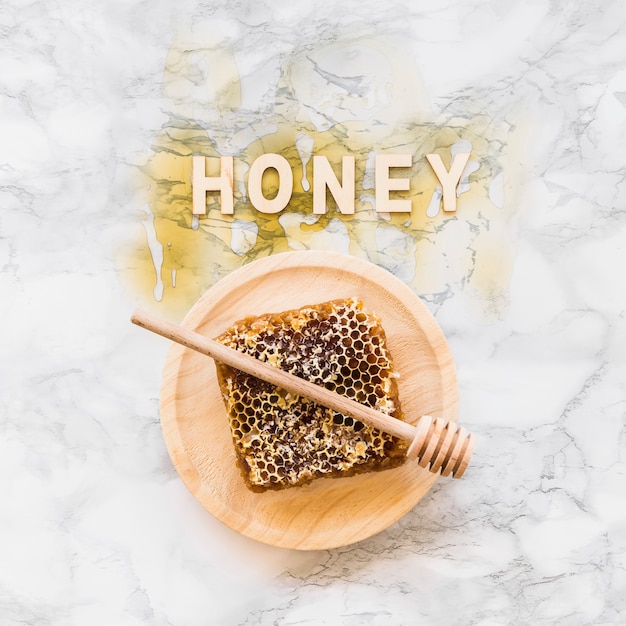 Free photo honey word over the honeycomb with dipper on wooden plate