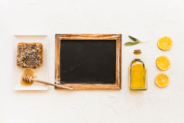 Foto gratuita favo, olio d'oliva e fette di limone con mestolo e ardesia vuota