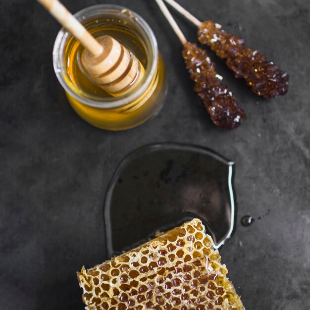 Honeycomb piece; honey pot and honey dipper on black texture backdrop