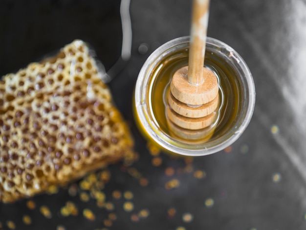 Honeycomb piece and honey pot with wooden dipper on black backdrop