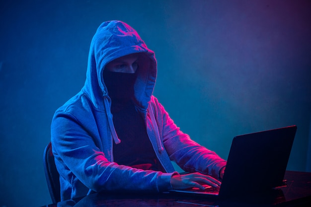 Hooded computer hacker stealing information with laptop