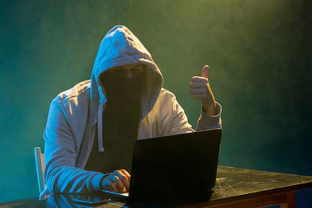 Free photo hooded computer hacker stealing information with laptop