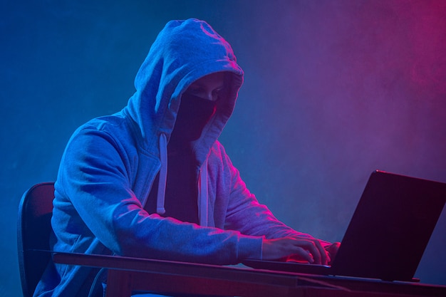 Hooded computer hacker stealing information with laptop