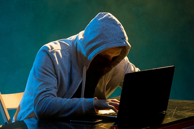 Hooded computer hacker stealing information with laptop