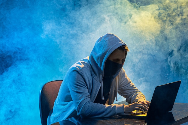 Компьютерный хакер с капюшоном ворует информацию с ноутбука