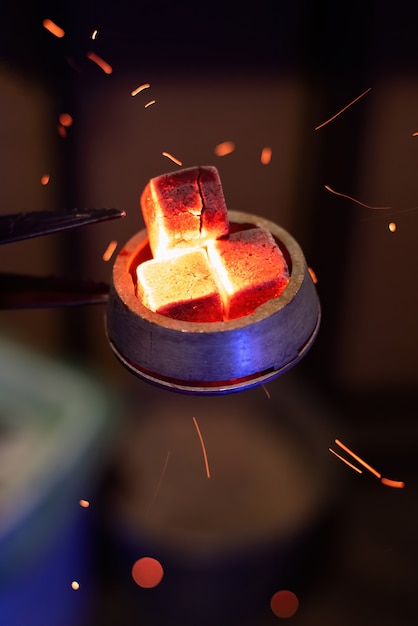 Hookah bowl with heated coals on it, particles flying around