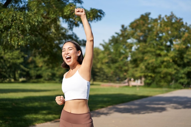 Hooray victory smiling asian girl triumphing celebrating achievement running till finish shouting