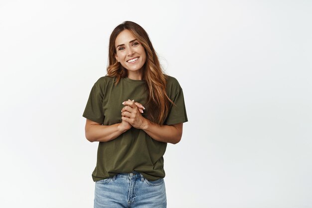 Hopeful ambitious woman smiling holding hands together waiting for results hope to get job wishing for smth standing in tshirt against white background