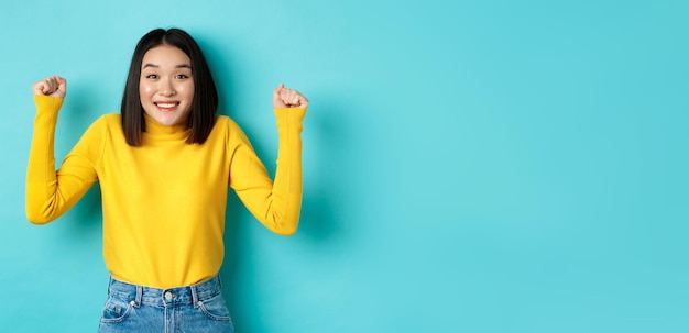 Free photo hopeful asian girl winning prize clench fists and smiling happy at camera triumphing of achievement