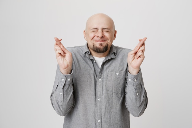 Hopeful bald guy cross fingers, making wish with closed eyes