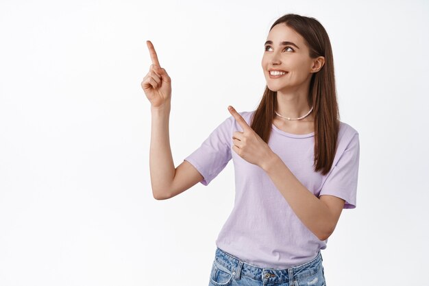 hopeful beautiful girl pointing, looking at upper left corner with happy smiling face with item on sale on white.