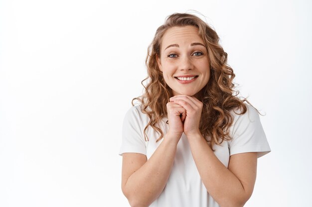 Hopeful cute blond girl looking at front with anticipation and hope, waiting for something, anticipating good thing, standing over white wall