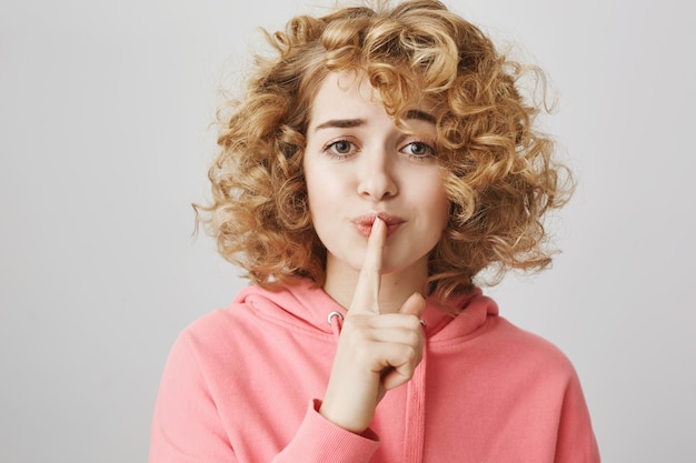 Free photo hopeful cute girl with curly hair hush, make shh gesture