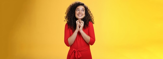 Foto gratuita speranzosa eccitata donna tenera carina in abito rosso con capelli ricci in piedi nuovo albero di natale che attraversa fing