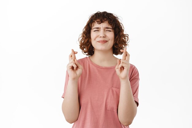 Hopeful girl cross fingers for good luck, making wish, standing over white background