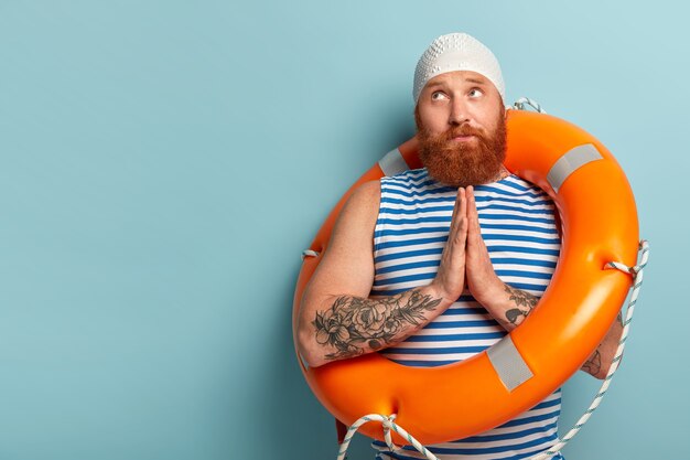 Обнадеживающий красивый пловец держит ладони вместе, молится о безопасном плавании, отдыхает на курорте, носит матросский жилет