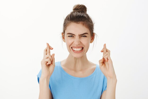 Hopeful intense young woman put effort into making wish, cross fingers good luck