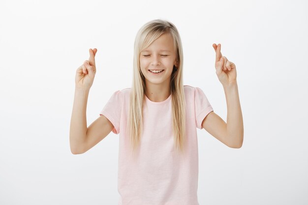 Hopeful little blond woman making wish, cross fingers good luck and smiling