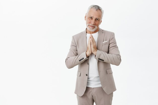 Hopeful old man in suit begging, holding hands in pray