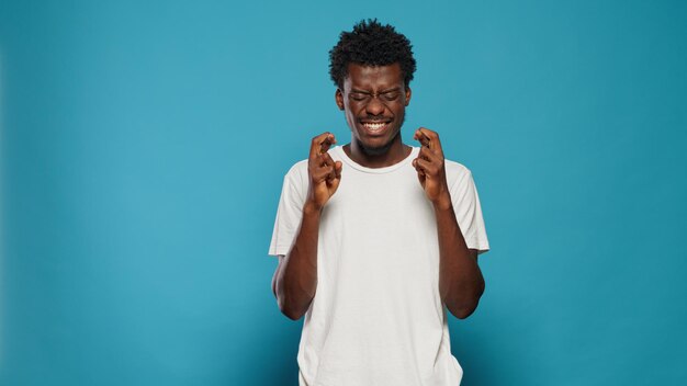 Hopeful person holding fingers crossed for good luck. Portrait of optimistic man doing gesture for prosperity and expected desire. Superstitious adult praying with lucky symbol