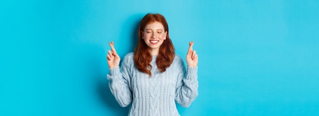 Free photo hopeful redhead girl making a wish cross fingers for good luck smiling and anticipating good news or