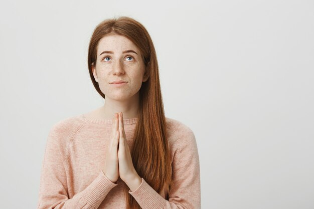 Hopeful redhead girl pleading God, hold hands in a prayer and looking up