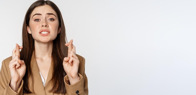 Free photo hopeful saleswoman corporate woman cross fingers and praying yearning to achieve smth standing in su