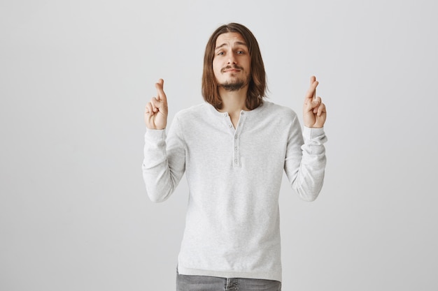 Hopeful smiling and optimistic guy cross fingers good luck, making wish