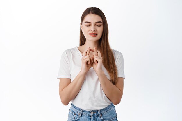 Hopeful stylish girl cross fingers for luck biting lip eager to receive positive result anticipating good news fortune making wish praying begging for dream come true white background