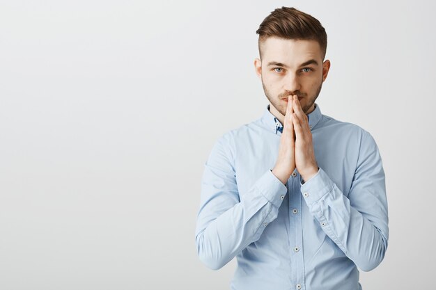 Hopeful worried businessman praying, holding hands in plead as awaiting results