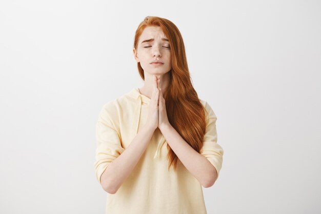Hopeful worried redhead girl hold hands in plead, praying