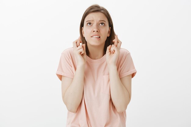 Hopeful worried woman begging God, praying or making wish with fingers crossed for good luck