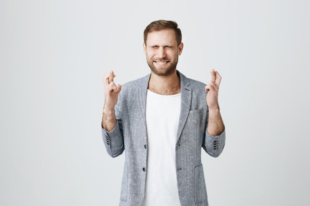 Hopeful young man pleading with closed eyes and crossed fingers