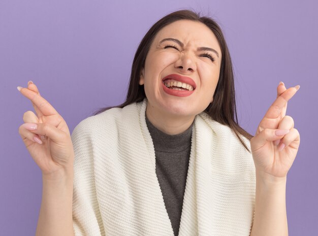 Hopeful young pretty woman doing good luck gesture looking up with one eye closed 