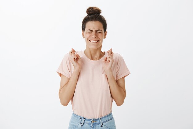 Hopeful young stylish woman posing against the white wall