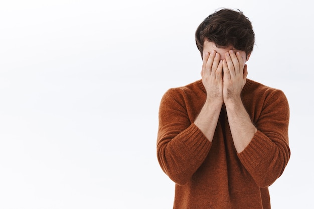 Free photo hopeless and desperate young tired man in sweatshirt, cover face with hands, feeling unwell