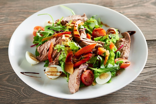 Horizontal close up shot of delicious freshly made salad with meat eggs and vegetables on the wooden table eating food lunch dinner meal gourmet mix chopped healthy edibles.