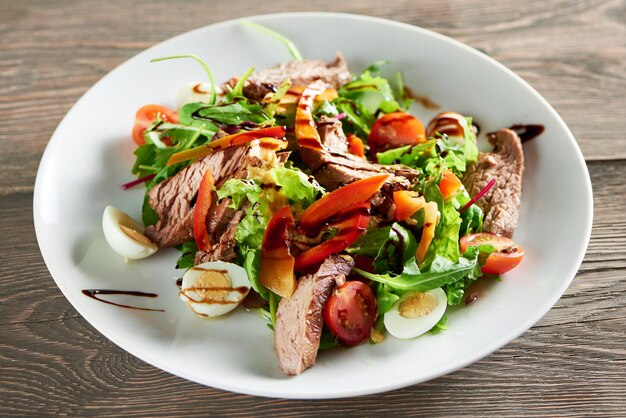 Horizontal close up shot of delicious freshly made salad with meat eggs and vegetables on the wooden table eating food lunch dinner meal gourmet mix chopped healthy edibles.