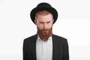 Free photo horizontal handsome elegant young red haired male with fuzzy beard squiring eyes and pursing lips, having suspicious look. unshaven man in hat and suit being displeased and angry