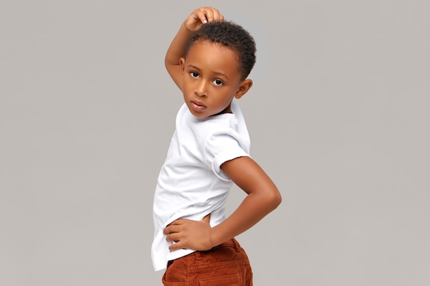 Horizontal image of handsome funny eight year old dark-skinned little boy posing isolated pretending to be fashion model,