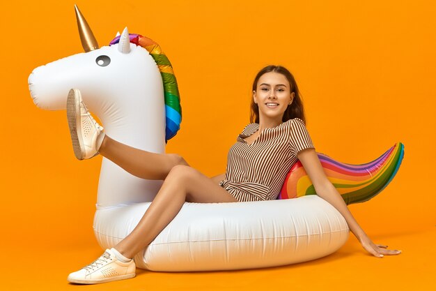 Horizontal image of overjoyed happy young Caucasian female in white sneakers and striped dress