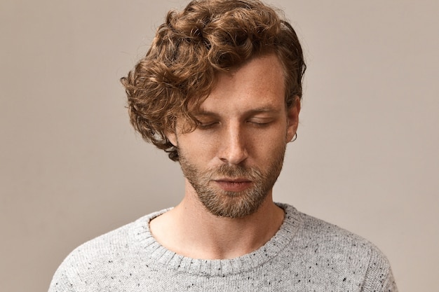 Free photo horizontal image of peaceful bearded good looking guy with voluminous reddish hair closing eyes, trying to concentrate on breathing, meditating. mindfulness, balance, harmony and peace concept