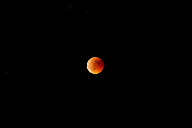 夜の暗い空にオレンジと赤の月の水平ロングショット