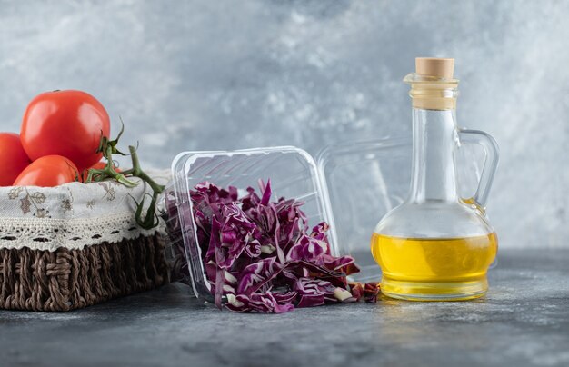 Horizontal photo of fresh tomatoes with chopped cabbage and bottle of oil on grey background. 