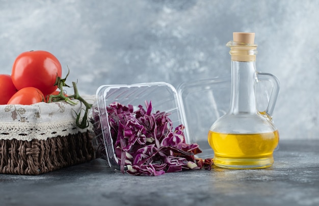 Horizontal photo of fresh tomatoes with chopped cabbage and bottle of oil on grey background. 