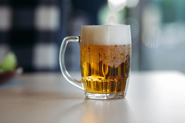 Horizontal photo of glass cup full of light fresh beer standing on smooth wooden surface Cold summer drink for day heat Fresh with thick high foam Blurred background Concept of drinks shooting