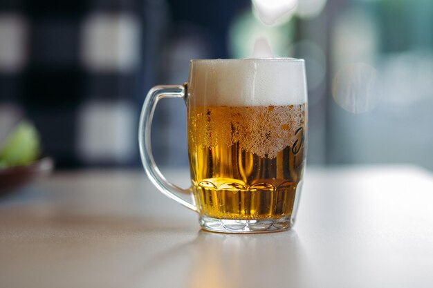 Horizontal photo of glass cup full of light fresh beer standing on smooth wooden surface Cold summer drink for day heat Fresh with thick high foam Blurred background Concept of drinks shooting