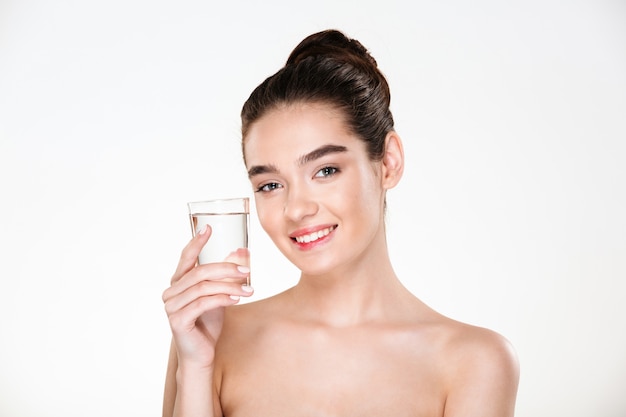 Horizontal picture of happy and healthy woman being half-naked drinking minaral water from transparent glass with smile